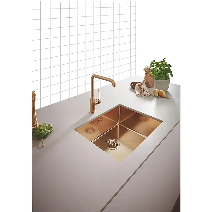 Grohe Essence Spültischarmatur - U-Auslauf, Warm Sunset, Matt - Moderne Küchenspüle aus Kupfer mit passender Armatur, eingebaut in eine helle Arbeitsplatte, vor weißem Fliesenspiegel.