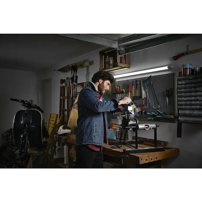 Osram LED-Lichtleiste Power Batten - L x B x H: 120 x 8,2 x 4,8 cm, Lichtfarbe: Warmweiß, 50 W, 220 V - 240 V - Werkstatt-Szene: Ein Mann arbeitet an einem Motor in einer gut ausgestatteten Garage mit Werkzeugen und einer Werkbank.