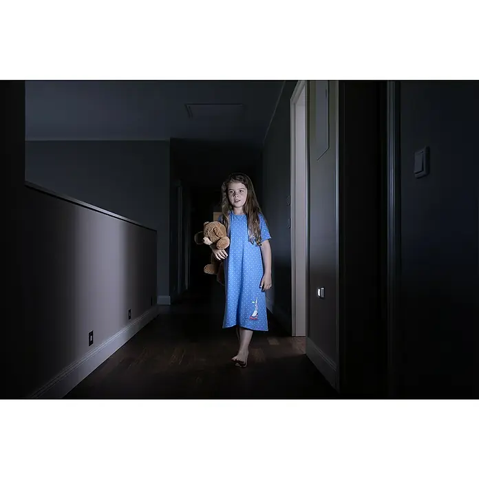 Osram Nightlux LED-Nachtlicht Hall - Silber, L x B x H: 8,4 x 7,3 x 2,2 cm - Ein kleines Mädchen mit einem Teddybär im Arm steht in einem dunklen Flur, beleuchtet durch ein dezentes Nachtlicht.