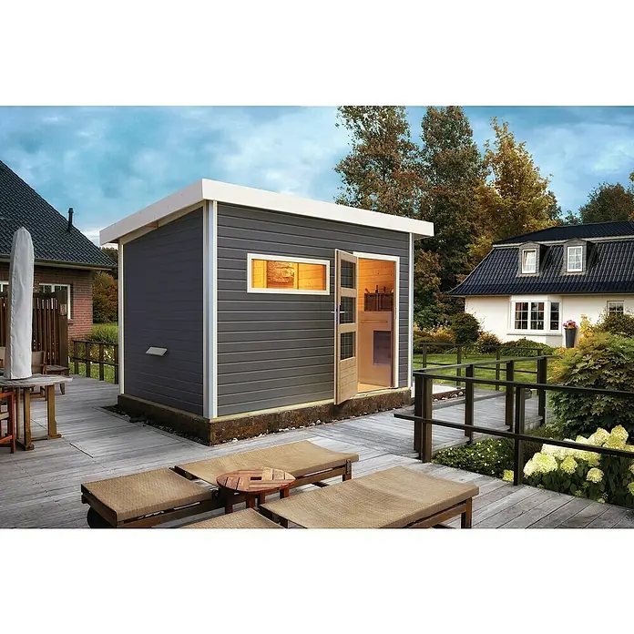 Karibu Saunahaus Danga - 9 kW Bio-Saunaofen mit externer Steuerung, Terragrau, L x B x H: 231 x 336 x 227 cm - Das Bild zeigt ein modernes Gartenhaus in Grau mit weißen Akzenten, das auf einer Holzterrasse steht und einen einladenden Eindruck vermittelt.