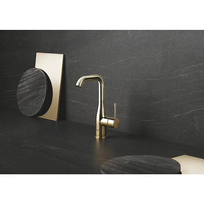 Grohe Essence New Waschtischarmatur L-Size - Mit Zugstange, Cool Sunrise, Glänzend - Nahaufnahme einer glänzenden goldenen Armatur auf einer dunklen Arbeitsfläche, die modernes Design und Eleganz ausstrahlt.