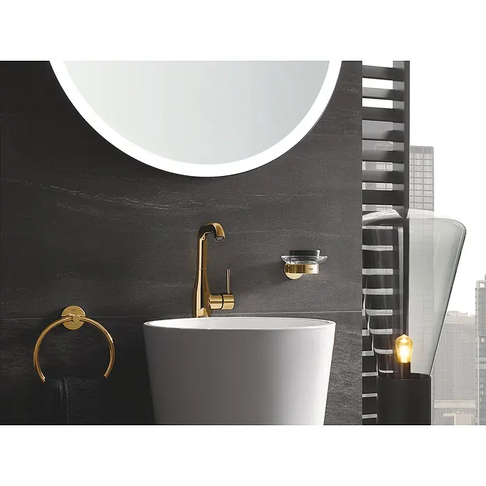 Grohe Essence New Waschtischarmatur L-Size - Mit Zugstange, Cool Sunrise, Glänzend - Nahaufnahme eines modernen Badezimmers mit goldenen Armaturen, einem runden Spiegel und einem stilvollen Waschbecken. Elegantes Design für ein luxuriöses Ambiente.