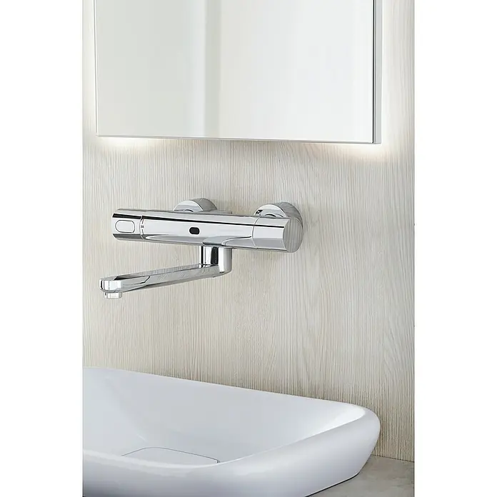 Grohe Eurosmart Cosmopolitan WaschtischarmaturInfrarot-Elektronik, Chrom, Glänzend, Ausladung: 287 mm - Eine Wandarmatur mit einem minimalistischen Design, die über einem modernen Waschbecken montiert ist, und einem integrierten Spiegel.