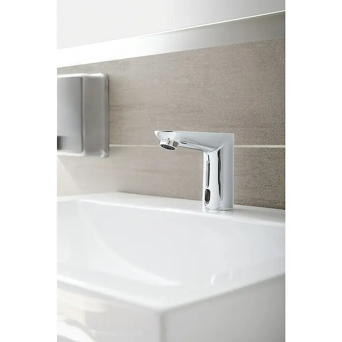 Grohe Euroeco CT Waschtischarmatur netzbetrieben - Infrarot-Elektronik, Chrom - Nahaufnahme eines modernen, berührungslosen Wasserhahns auf einem weißen Waschbecken mit einer hellgrauen Wand im Hintergrund.