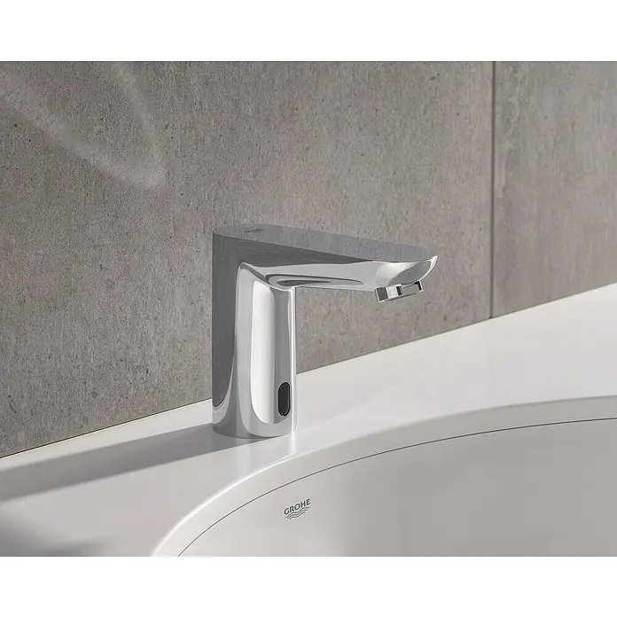 Grohe Euroeco CT Waschtischarmatur batteriebetrieben - Infrarot-Elektronik, Chrom - Nahaufnahme eines glänzenden, modernen Grohe Wasserhahns auf einem weißen Waschbecken vor einer grauen Wand.