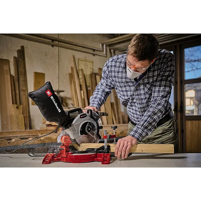Einhell Kapp- & Gehrungssäge TC-MS 2112 - 1.600 W, Durchmesser Sägeblatt: 210 mm, Leerlaufdrehzahl: 5.000 U/min - Ein Mann mit Schutzbrille und Mundschutz arbeitet mit einer Einhell Kapp- und Gehrungssäge an einem Holzstück.