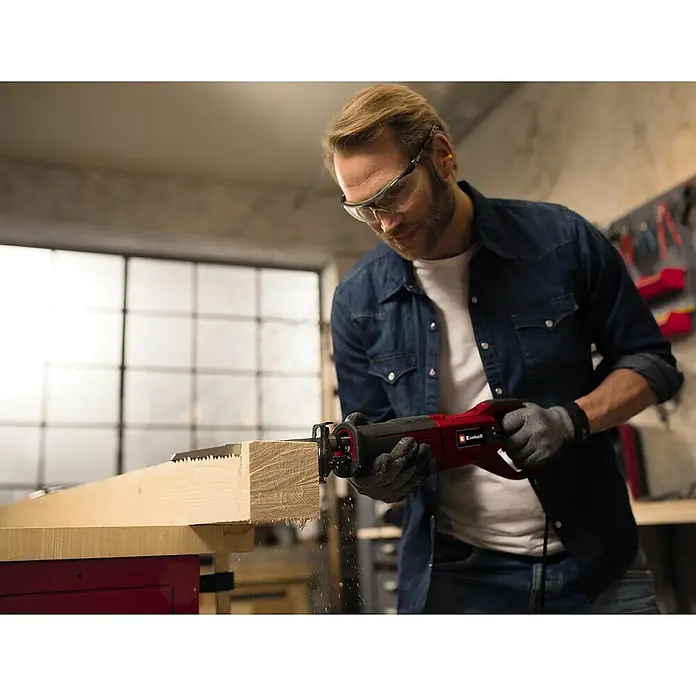 Einhell Expert Säbelsäge TE-AP 950 E950 W - Ein Mann sägt mit einer Einhell Säbelsäge ein Holzbrett, wobei er Schutzbrille und Handschuhe trägt.