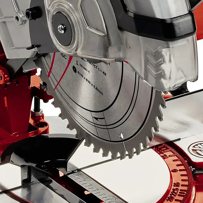 Einhell Sierra ingletadora TC-MS 2112 - 1.600 W, Diámetro hoja de sierra: 210 mm, Número de revoluciones de marcha en vacío: 5.000 r.p.m. - Primer plano de una sierra circular con protección de seguridad, destacando detalles como las marcas de la hoja y la estructura de los dientes.