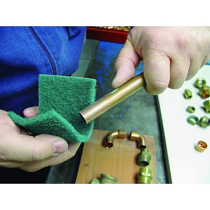 Tubo de cobre - Diámetro: 12 mm, Largo: 2,5 m - Primer plano de una persona limpiando una tubería de cobre con un estropajo verde, con varios accesorios de plomería en la mesa.