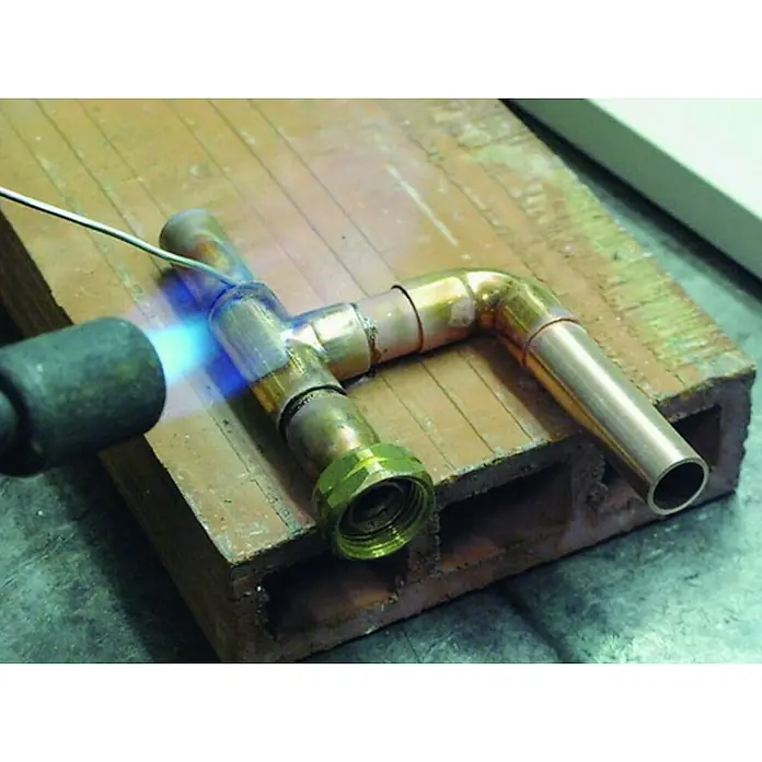 Racor loco - Rosca interior: ½″, 18 mm, Cobre, Dorado - Primer plano de la soldadura de una conexión de tubería de cobre con un soplete y soldadura sobre una superficie ignífuga para garantizar una conexión sólida y estanca.