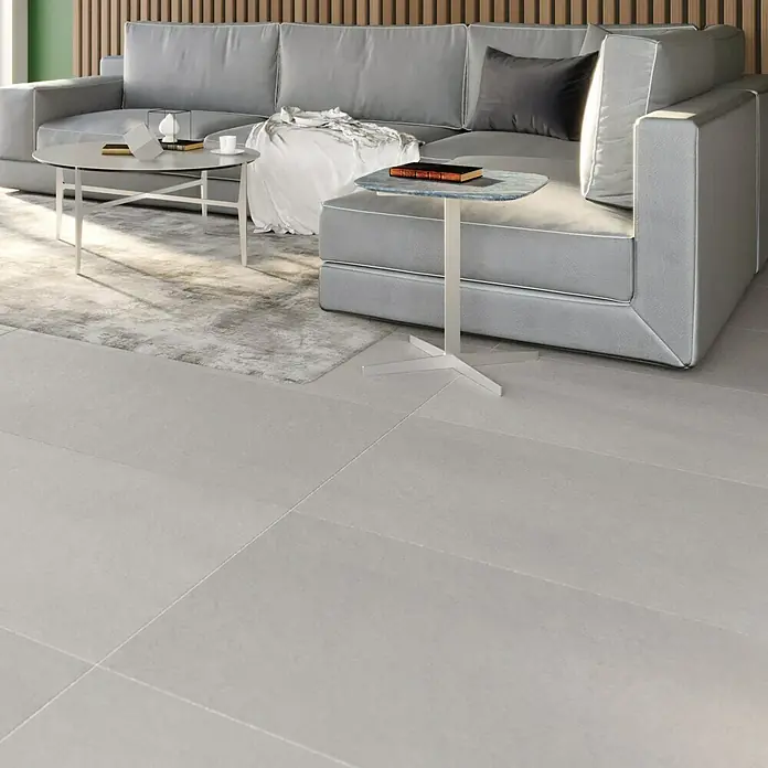 Ambiente by Palazzo Feinsteinzeugfliese - 60 x 120 cm, Grau, Matt - Großes graues Sofa mit Kissen und Beistelltisch auf einem hellen Teppich und Fliesenboden. Moderne Inneneinrichtung für Wohnräume.