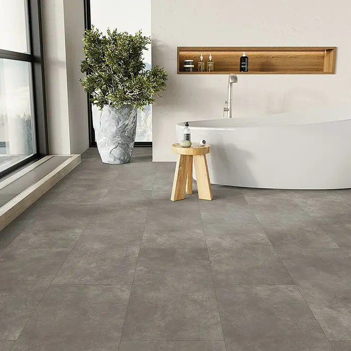 Parador Designbodenmuster Modular ONE Beton dunkelgrau - 200 x 202 x 8 mm, Fliesenoptik - Helle Badezimmergestaltung mit Badewanne, Holzhocker und großem Fenster für ein entspannendes Ambiente.