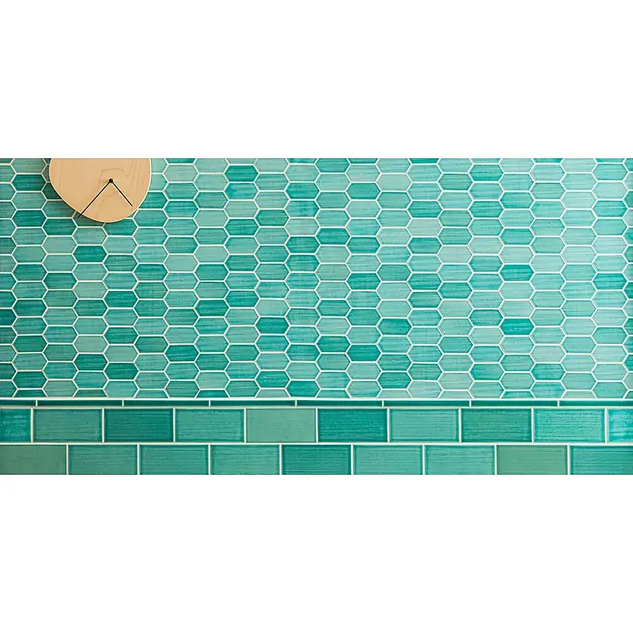 Mosaikfliese Hexagon CG CH475 - Grün, Glänzend, 25,3 cm x 29,3 cm x 75 mm - Detailaufnahme einer Wand mit türkisfarbenen Sechseckfliesen und rechteckigen Bordüren, ergänzt durch eine helle Holzuhr.