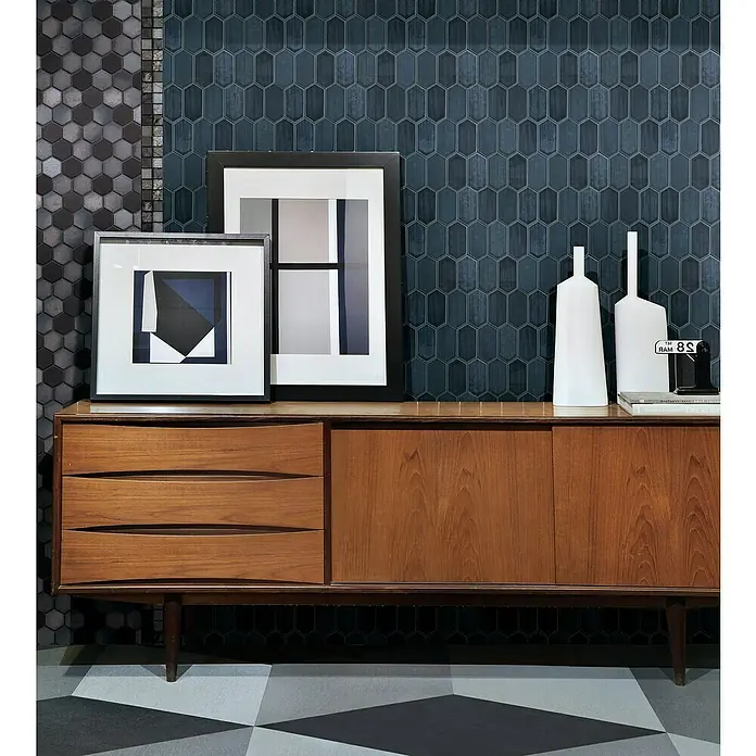 Mosaikfliese Hexagon CG CH479 - Schwarz, Glänzend, 25,3 cm x 29,3 cm x 75 mm - Ein Sideboard aus Holz mit Schubladen und Schiebetüren, dekoriert mit Kunst, Vasen und Büchern, vor einer Wand mit geometrischen Mustern.