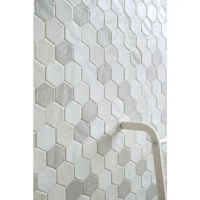 Mosaikfliese Hexagon CG SAN1 - Weiß, Glänzend, L x B x S: 25,3 cm x 29,3 cm x 7 mm - Nahaufnahme einer Wand mit hellgrauen und weißen sechseckigen Fliesen, die ein modernes und stilvolles Design zeigen.