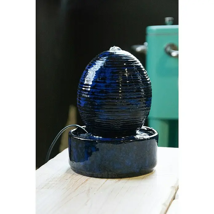 Dobar Zimmerbrunnen Kugel - L x B x H: 17 x 17 x 21 cm - Nahaufnahme eines stilvollen blauen Keramik-Tischbrunnens auf einer hellen Holzoberfläche, der einen ruhigen und dekorativen Akzent setzt.