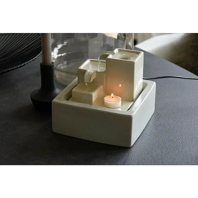 Dobar Zimmerbrunnen - 19 x 19 x 16,5 cm, Keramik - Nahaufnahme eines Indoor-Tischbrunnen mit fließendem Wasser und einer brennenden Kerze für eine entspannende Atmosphäre.