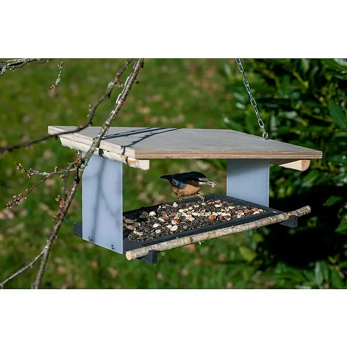 Dobar Vogelfutterhaus Futura II - 38 x 22 x 18 cm, Weiß, Holz - Eine Nahaufnahme eines Vogelhauses mit einem niedlichen Kleiber, der einen Samen im Schnabel hält. Das Vogelhaus ist mit allerlei Futter gefüllt.