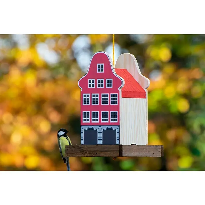 Dobar Vogelfutterhaus - 19 x 19 x 30 cm, Natur/ Rosa, Holz - Ein farbenfrohes Vogelhaus in Hausform mit einer Kohlmeise auf der Holzstange. Das Haus hat eine rote Fassade mit weißen Fenstern und ein rotes Dach.