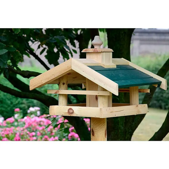 Dobar Vogelfutterhaus Kulusuk - 43 x 40 x 32 cm, Natur/ Grün, Holz - Ein detailreiches Foto eines hölzernen Vogelhauses mit grünem Dach, platziert in einem Garten mit üppigem Grün und blühenden rosa Blumen.