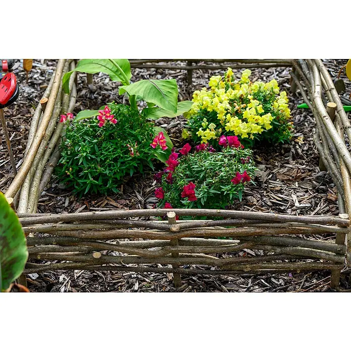 Dobar Beeteinfassung 4er Set - Haselnuss - Ein charmantes, kleines Gartenbeet mit einem rustikalen Zaun aus Ästen, bepflanzt mit bunten Blumen in Gelb- und Rottönen, die eine idyllische Szene schaffen.
