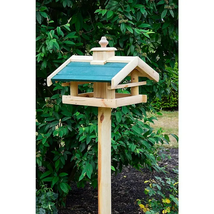 Dobar Vogelfutterhaus Kulusuk - 43 x 40 x 32 cm, Natur/ Grün, Holz - Ein hölzernes Vogelhaus mit grünem Dach steht auf einem Pfosten im Garten, umgeben von üppigem Grün. Das dekorative Häuschen bietet einen sicheren Futterplatz für Vögel.