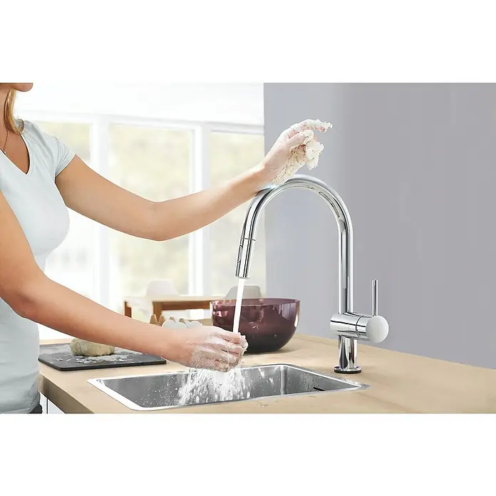 Grohe Spültischarmatur Minta Touch 2 - Chrom, Glänzend - Moderne Chromarmatur mit hohem Auslauf. Eine Frau wäscht ihre Hände unter dem fließenden Wasserhahn in einer hellen Küche.