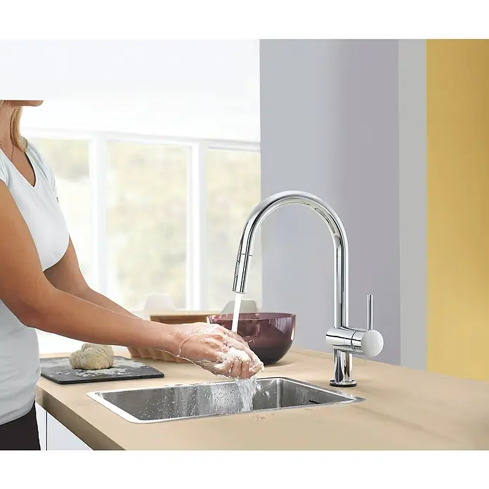 Grohe Spültischarmatur Minta Touch 2 - Chrom, Glänzend - Frau wäscht sich die Hände an einem modernen Chrom-Küchenarmatur mit Einhebelmischer und Ausziehbrause in einer hellen Küche.