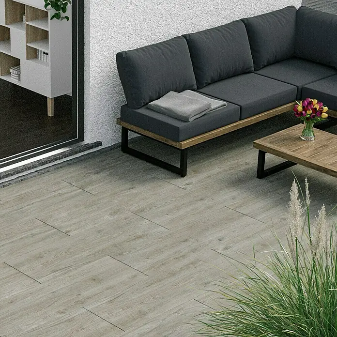 Marazzi Terrassenfliese Esterno 20T Woodliving Fumo - 40 x 120 x 2 cm, Beige, Matt - Das Bild zeigt eine moderne Terrasse mit grauen Fliesen in Holzoptik, die einen stilvollen Außenbereich schaffen. Eine graue Eckcouch lädt zum Verweilen ein.