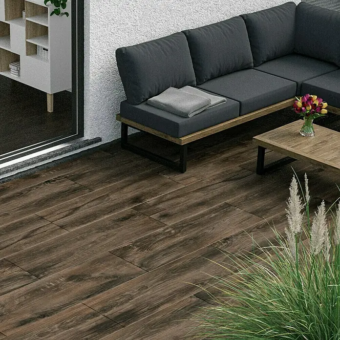 Marazzi Terrassenfliese Esterno 20T Trevermade - 40 x 120 x 2 cm, Zeder, Matt - Dunkle Holzterrasse mit komfortabler Eckcouch und Tisch, ideal für den Außenbereich. Elegantes Design für entspannte Stunden.
