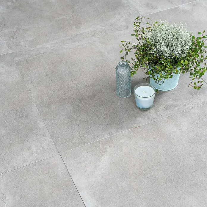Diephaus Terrassenfliese Columbia - 60 x 60 x 4 cm, Concreto Quarzit, Beton - Einrichtungselement mit Bodenfliesen, einer Vase, einer Kerze und einer Topfpflanze, die ein entspannendes und ästhetisches Ambiente erzeugen.