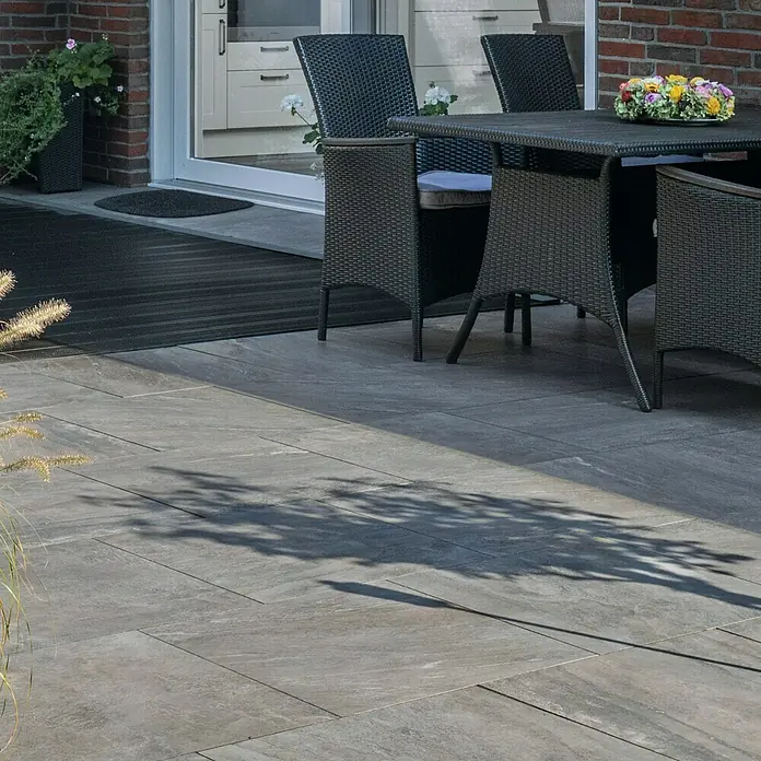 Diephaus Terrassenfliese Columbia - 60 x 60 x 4 cm, Basalt, Beton - Bild einer Terrasse mit modernem Steindesign. Elegante Gartenmöbel aus Rattan ergänzen das stilvolle Ambiente des Außenbereichs.