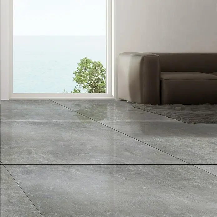 Feinsteinzeugfliese Luna Gris120 x 240 cm, Grau, Schimmernd - Innenraum mit glänzenden, grauen Bodenfliesen, einem beigen Sofa und einem Fenster mit Meerblick. Elegantes und modernes Design.