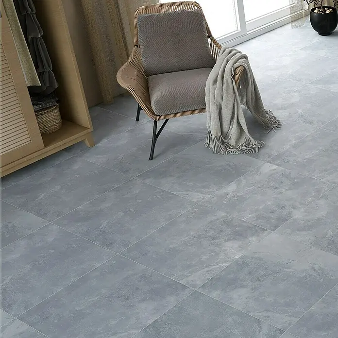 Feinsteinzeugfliese Geo Grey - 60 x 60 cm, Grau, Schimmernd - Eine Nahaufnahme von grauen Bodenfliesen, die einen modernen Raum mit einem Stuhl und einem Schrank ergänzen. Das Fliesenmuster verleiht dem Raum Eleganz.
