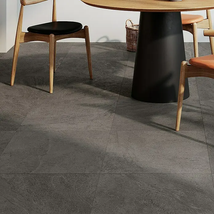 Atlas Concorde Solution Terrassenfliese Island Black - 60 x 60 x 2 cm, Schwarz, Matt - Nahaufnahme von dunklen Bodenfliesen unter einem Esstisch mit Stühlen, die ein modernes und stilvolles Ambiente schaffen.