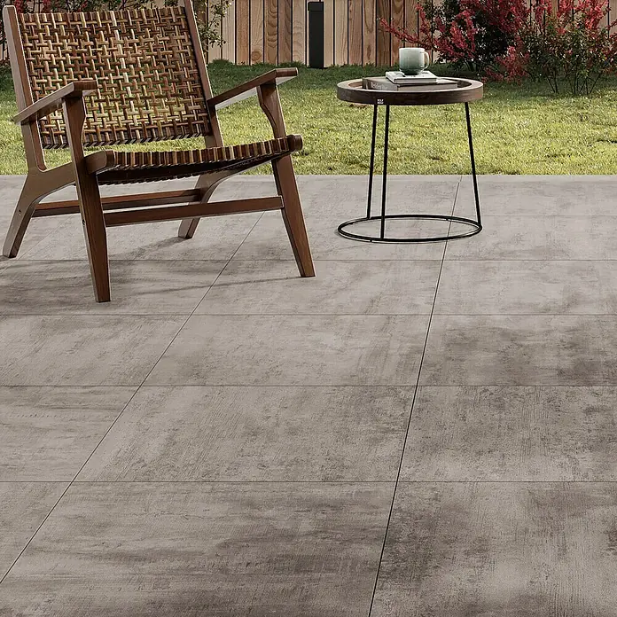 Atlas Concorde Solution Terrassenfliese Rover Grey - 60 x 60 x 2 cm, Grau, Matt - Terrassenansicht mit großformatigen Bodenfliesen in Betonoptik, die einen modernen und stilvollen Außenbereich schaffen. Sessel und Beistelltisch ergänzen das Ambiente.