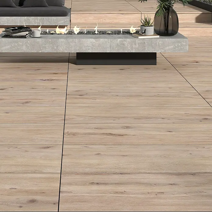 Terrassenfliese Garden Coldbrown 2.0 - 39,7 x 119,7 x 2 cm, Grau/Braun, Matt - Außenaufnahme mit einem modernen Terrassenbereich, der mit Holzdielen ausgelegt ist und einen stilvollen Feuerstellentisch aus Beton beinhaltet.