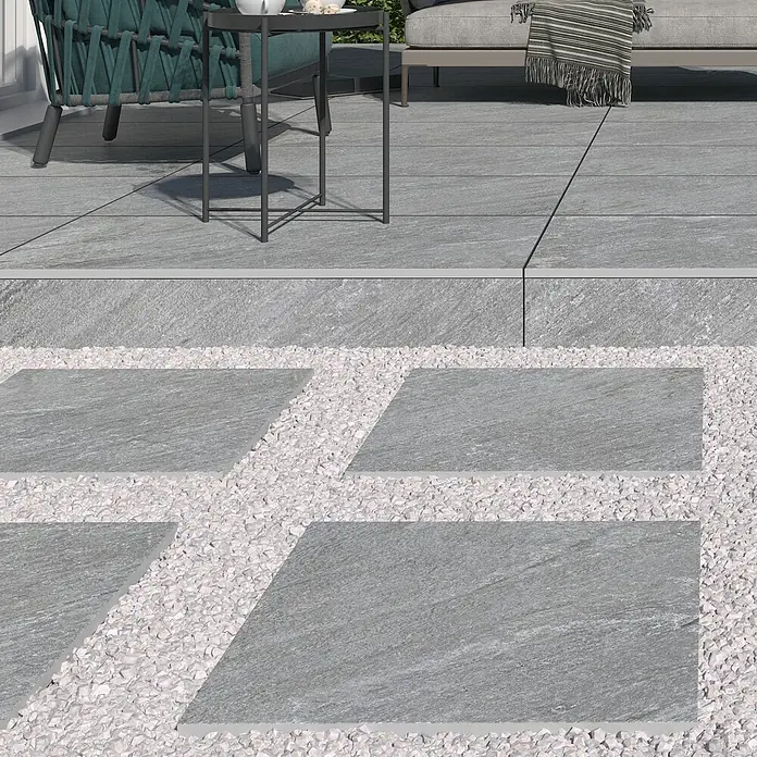 Terrassenfliese Piazza 2.0 - 59,7 x 59,7 x 2 cm, Grau, Matt - Ein stilvoller Außenbereich mit grauen Terrassenplatten und weißen Kieselsteinen, perfekt für moderne Gärten und Entspannung.