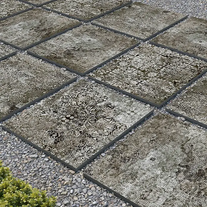 Terrassenfliese Persian Black 2.0 - 60 x 60 x 2 cm, Schwarz, Matt - Ein Feld mit dekorativen quadratischen Bodenfliesen, umgeben von Kies, ideal für den Außenbereich.