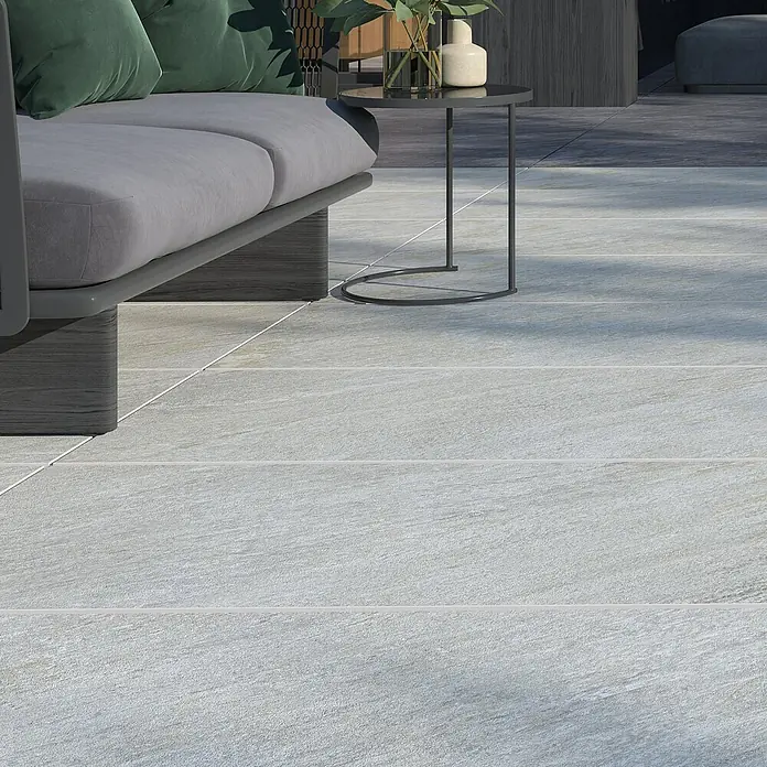 Terrassenfliese Piazza 2.0 - 59,7 x 119,7 x 2 cm, Sabbia, Matt - Nahaufnahme von grauen Terrassenfliesen mit subtiler Textur, die einen modernen Außenbereich mit Sitzgelegenheiten ergänzen.
