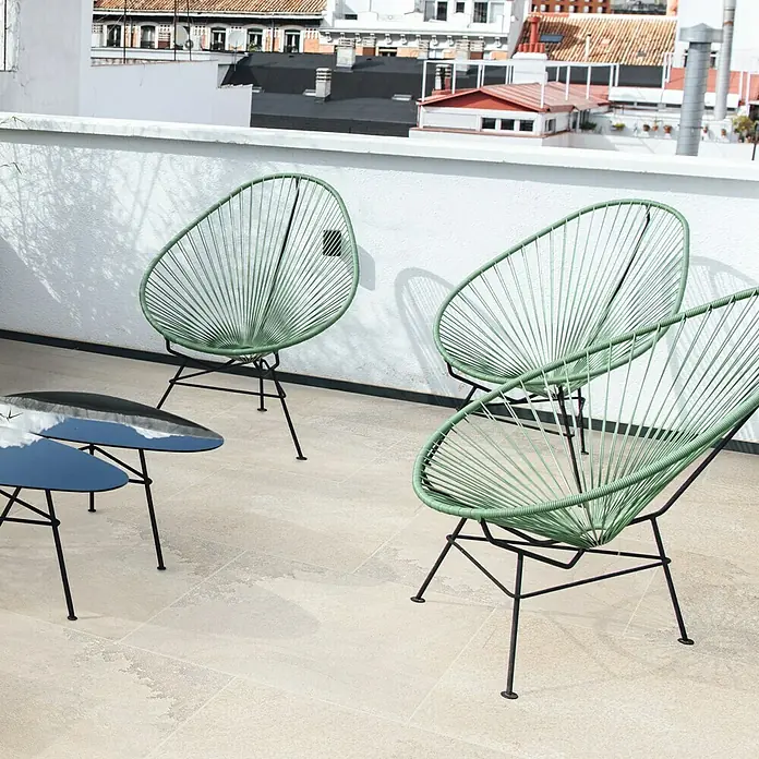 Terrassenfliese Jura 2.0 - 60 x 60 x 2 cm, Beige, Matt - Eine Terrasse mit drei modernen Acapulco-Stühlen in Mintgrün und einem schwarzen Couchtisch. Die Stühle laden zum Verweilen im Freien ein.