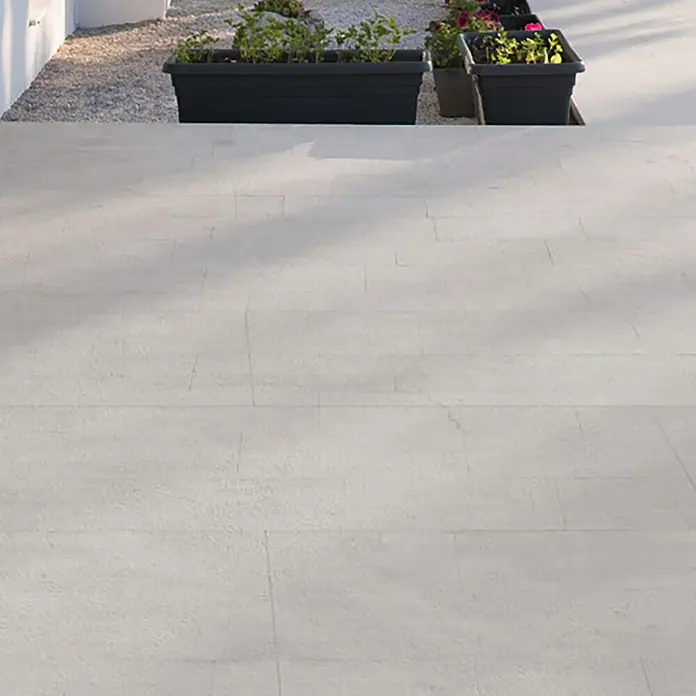 Terrassenfliese Revesto 2.0 - 60 x 60 x 2 cm, Grau, Matt - Detailaufnahme von Pflanzkästen mit üppigem Grün und bunten Blumen auf einem hellen, gepflasterten Untergrund.