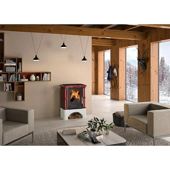 Justus Kaminofen Bavaria - 7 kW, Raumheizvermögen: 144 m³, Material Verkleidung: Keramik, Bordeaux - Wohnzimmer mit rotem Kaminofen mit Holzscheiten, flankiert von hellgrauen Sesseln und dekorativen Regalen.