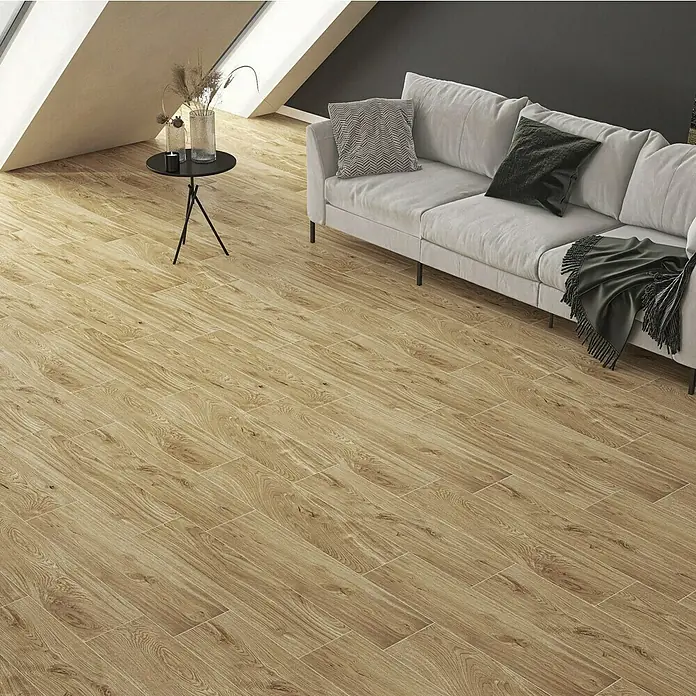 Atlas Concorde Solution Feinsteinzeugfliese Kortex Golden22,5 x 90 cm, Hellbraun, Matt - Ein modernes Wohnzimmer mit Holzbodenfliesen in warmen Brauntönen, einem grauen Sofa, einem Beistelltisch und großen Fenstern.