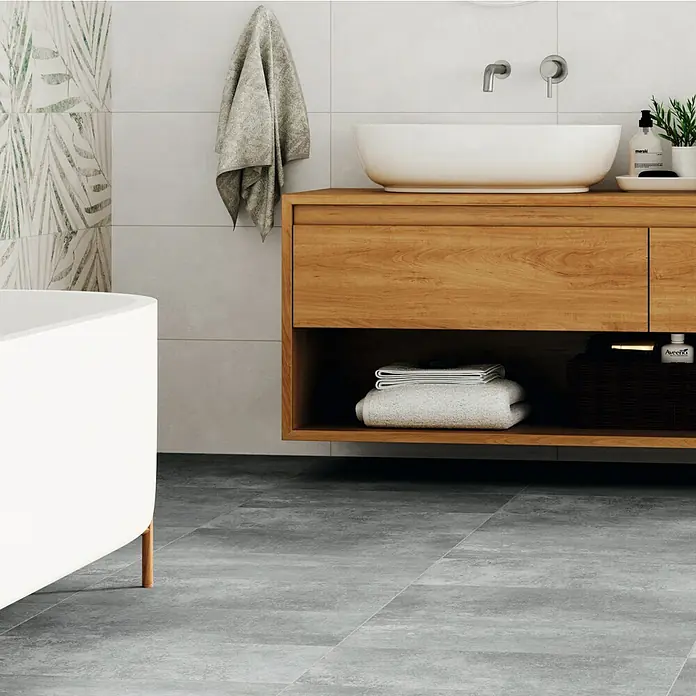 Domicil Feinsteinzeugfliese Living Concrete - 30 x 60 cm, Grau, Matt - Das Bild zeigt ein modernes Badezimmer mit einem Waschtisch aus Holz, einem ovalen Waschbecken und grauem Fliesenboden. Ein hängendes Handtuch ergänzt das Arrangement.