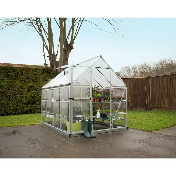 Palram – Canopia Invernadero Hybrid - Medidas ext. (An x Pr): 185 x 248 cm, Plateado, Área: 4,6 m² - Un invernadero espacioso con plantas y herramientas de jardinería, situado en un camino de jardín pavimentado, ideal para cultivar.