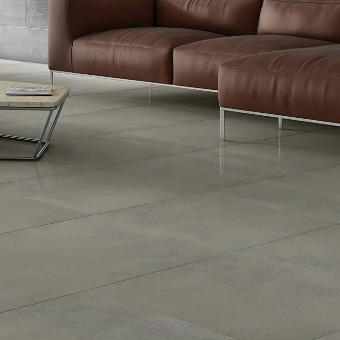 Art-Tec by Palazzo Feinsteinzeugfliese - 59,5 x 59,5 cm, Clay, Glänzend - Detailaufnahme eines modernen Wohnraums mit grauen Bodenfliesen und einem braunen Ledersofa. Stilvolles Design für ein elegantes Ambiente.