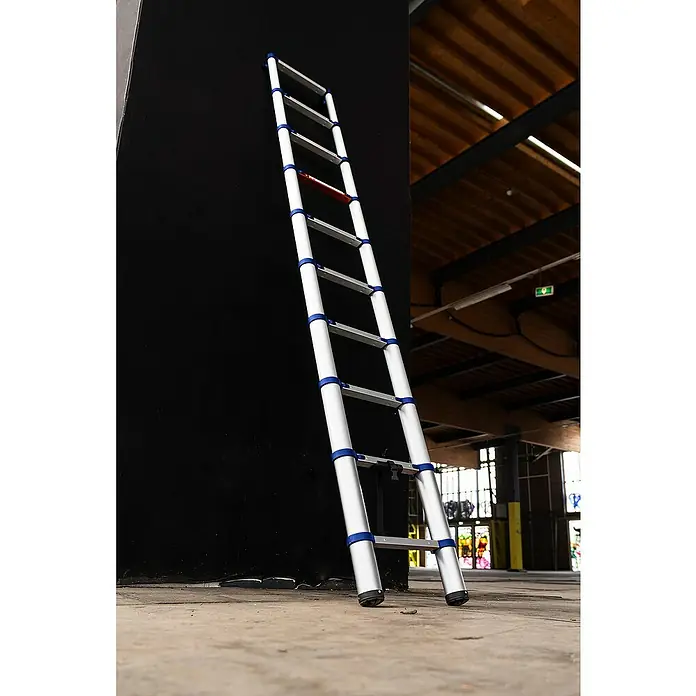 Stabilomat Teleskopleiter - Arbeitshöhe: 3,63 m, Aluminium - Eine ausziehbare Aluminiumleiter mit blauen Akzenten lehnt an einer schwarzen Wand.