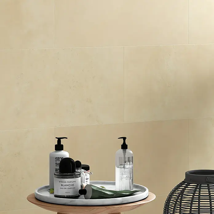 Art-Tec by Palazzo Feinsteinzeugfliese - 60 x 120 cm, Creme, Glänzend - Ein Arrangement von Badezimmerartikeln auf einem kleinen Tisch, darunter Seife, Parfüm und eine Tube Creme, vor einem beigen Hintergrund.