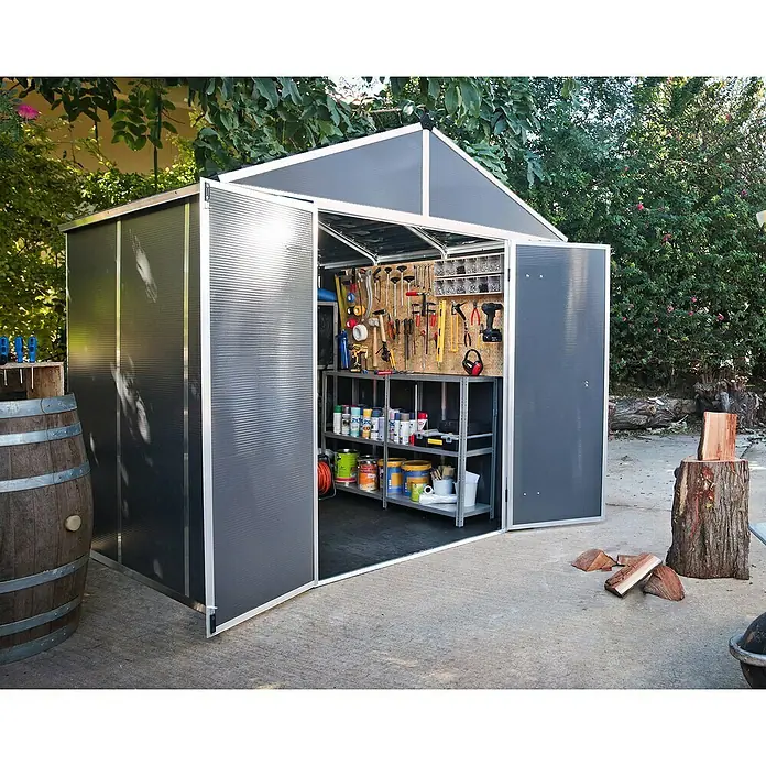 Palram – Canopia Caseta de jardín Rubicon - Medidas ext. (An x Pr): 237 x 229 cm, Plástico, Antracita - La imagen muestra un cobertizo de jardín gris con puertas abiertas, donde se guardan herramientas y pinturas. En primer plano hay un barril de madera.